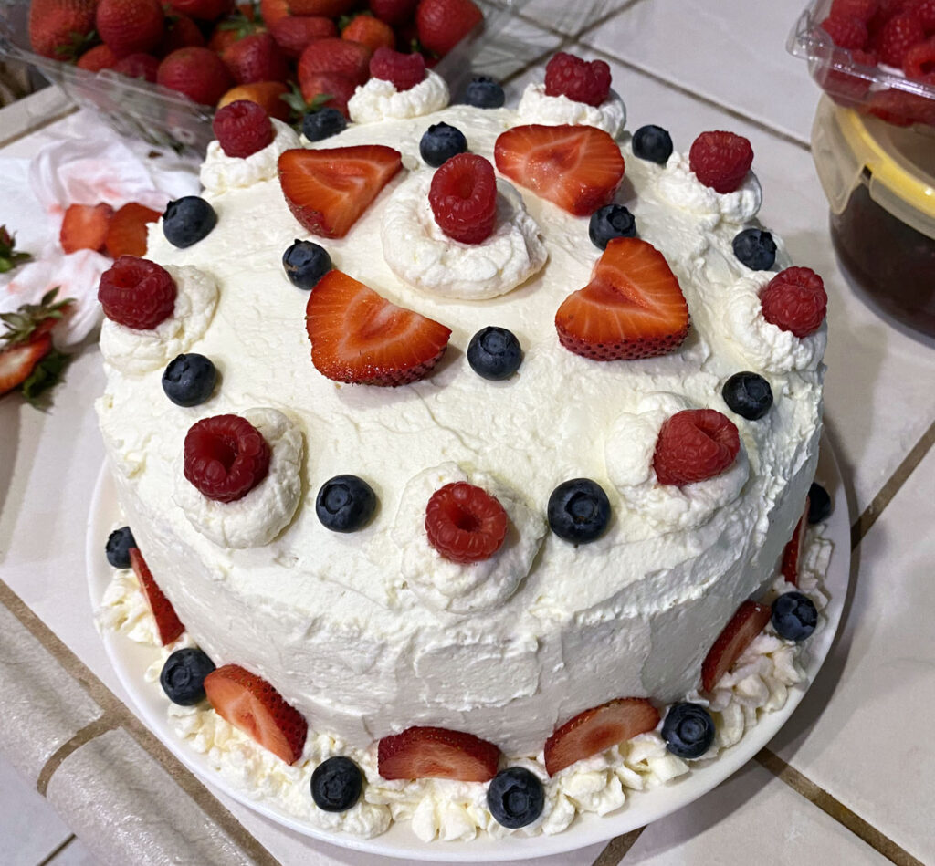 Picture of a cake with buttercream frosting, decorated with summer berries.