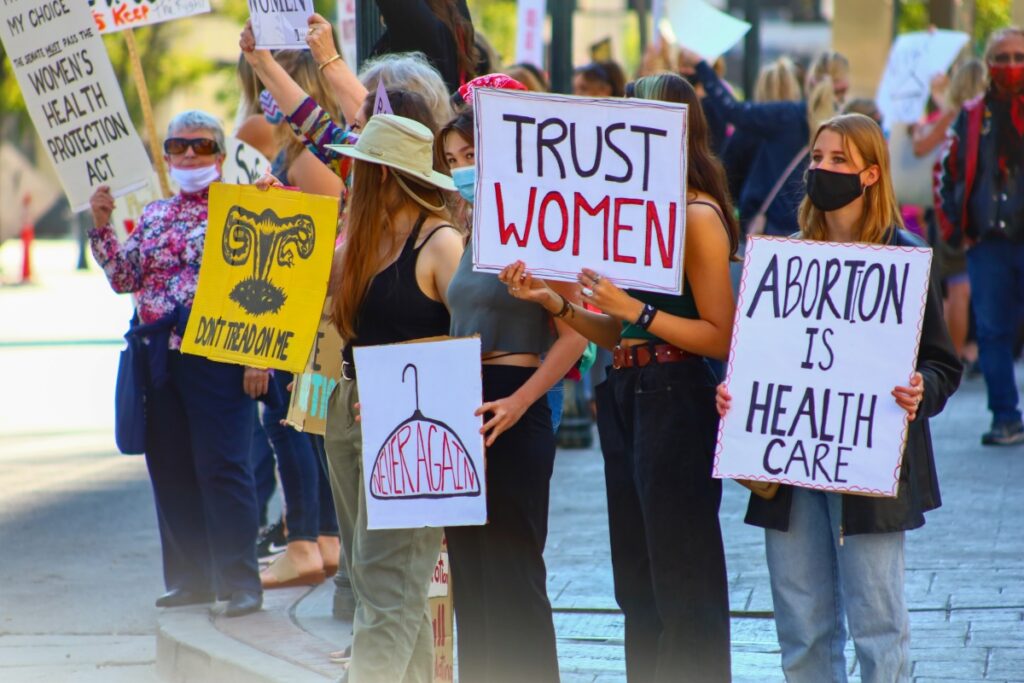 Photo of a protest about abortion rights. Signs read "Trust Women" and "Abortion is Health Care" and "Don't Tread on Me."